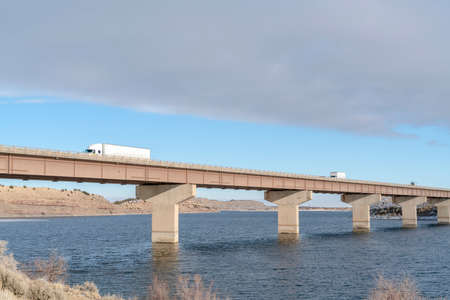Huge trucks travelling on a massive bridge against snowy hills and cloudy sky. The infrastructure...