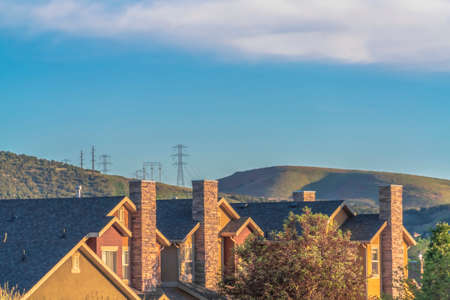 Homes with gray gable roofs and stone brick chimneys against mountain and sky. Sunny day views of...