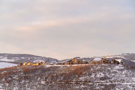 Homes on grassy and snowy hills against cloudy sky on a frosty winter day. The residential...