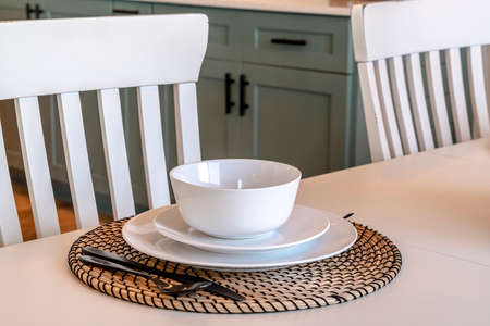 Dining table setting of home against chairs wooden floor and kitchen cabinets. Soup bowl, saucer,...