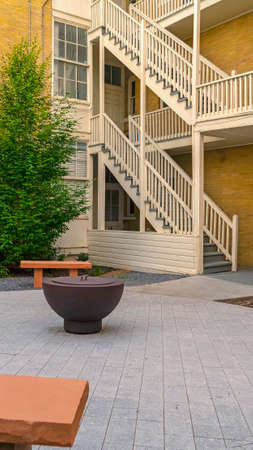 Vertical Fire pit on circular pavement with stone benches against building exterior. Residential...