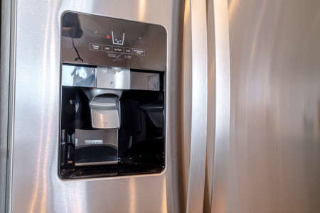 Water and ice dispenser on the shiny door of a refrigerator inside a home. A modern electrical...