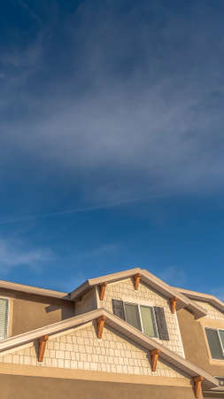Vertical Home with front gable roof and dormers against vast blue sky with clouds. Upper storey of a...