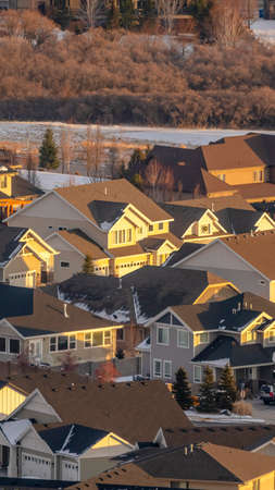 Vertical frame Houses with snow covered yards along paved roads viewed in winter. Neighborhood landscape illuminated by sunlight on a cold and sunny day.の写真素材