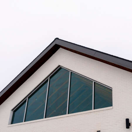 Photo Square frame Home exterior with tringular window and white wall under gable roof. The roofs of...