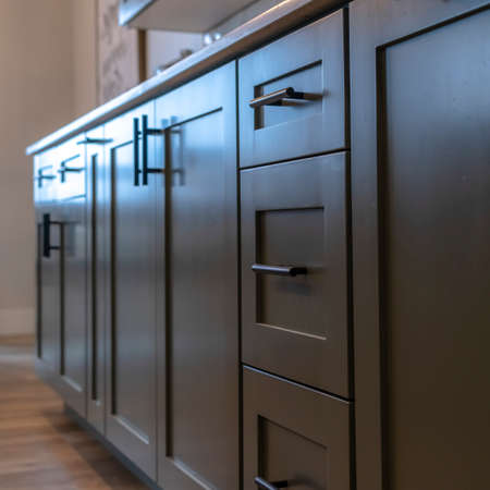 Square Beautiful cabinetry with black handles and drawers under white countertop. Wooden floor, hanging wall cabinets, dining table, and chair can also be seen inside this room.の写真素材