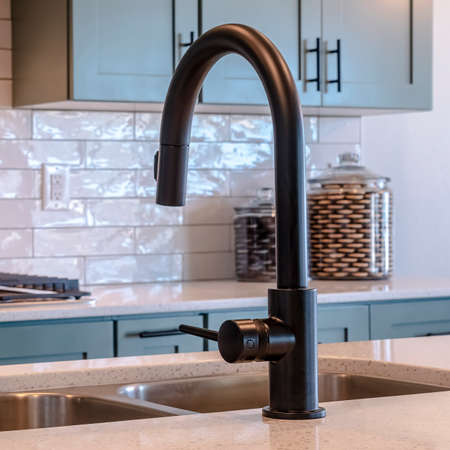 Photo Square frame Black faucet and double bowl kitchen island sink against cooktop and cabinets. Tile backsplash and white wall cna also be seen in the background.の写真素材