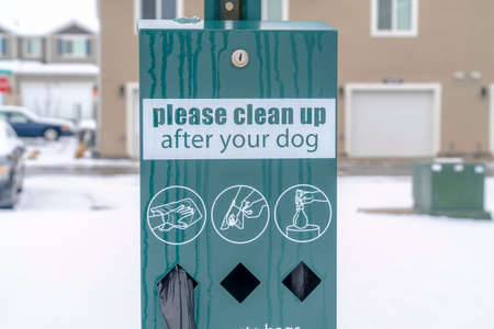 Pet Waste Station with black dog poop bags against blurry homes and snowy ground