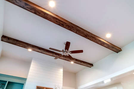 Wood beams and recessed bulbs with ceiling fan and lights at the center. Living room interior of home with close up view of the lighting and ventilation fixtures at the ceiling.の写真素材