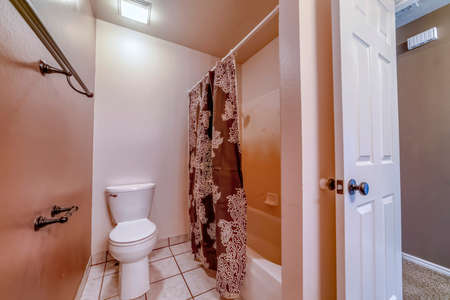 Toilet and bathtub inside bathroom with tile floor and wall mounted towel rods. Printed shower curtain and open door cna also be seen inside the room.の写真素材