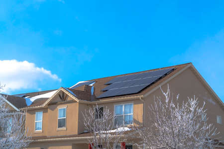 Home along Wasatch Mountain terrain with solar panels on the pitched roof. Frosted leafless trees and bright blue sky can also be seen in this neighborhood.の写真素材