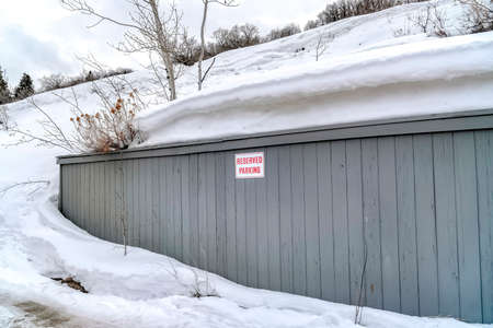 Gray wooden wall with Reserved Parking sign against snowy hill and sky in winter. Signage at a parking area surrounded by snow covered nature landscape.の写真素材
