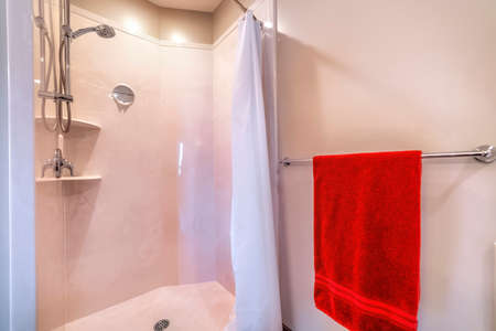 Shower area with stainless steel shower head tile wall curtain mirror and racks. Bright red towel is hanging on a wall-mounted metal rod.の写真素材