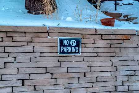No Parking sign on a stone brick retaining wall topped with snow in winter. Signage that prohibits parking viewed against snowy views on a cold day.の写真素材