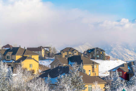Houses on snow covered Wasatch Mountain setting on a sunny winter day. The town has a scenic view of towering frosted peaks beneath cloudy blue sky.の写真素材