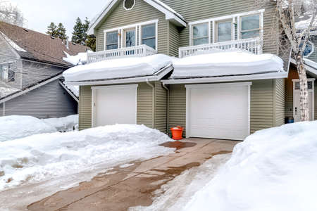 Facade of home with snowy driveways in front of two car garage viewed in winter. Pitched roof, gray wall siding, and balconies can also be seen at the exterior of this house.の写真素材