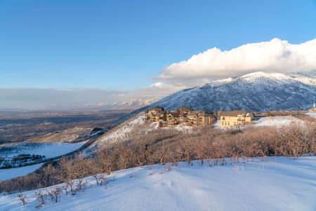 Wasatch Mountains landscape in winter with houses sitting on the snowy slope. Vast valley and blue sky with puffy clouds can be seen on this sunny scenery.の写真素材