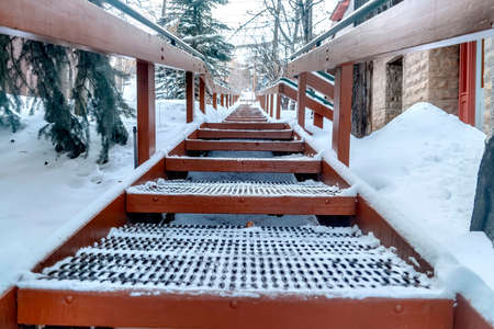 Focus on grate metal treads of outdoor stairs against snowy hill in winter. The stairway has a...