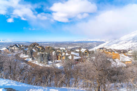 Wasatch Mountains in winter with homes on a neighborhood amid nature scenery. Vast residential valley and cloudy blue sky can also be seen in this winter landscape.の写真素材