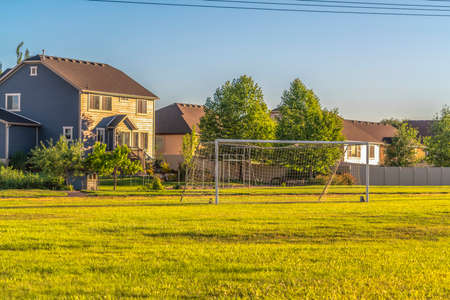 Soccer goal on vast green grassy field in front of houses viewed on a sunny day. Football or soccer field at a scenic residential neighborhood under blue sky.の写真素材
