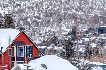Houses in snowy Park City Utah mountain with abundant trees in the background. A home with pitched roof over vibrant red wall can be seen in the foreground.の写真素材