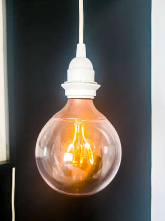 Electric light bulb with white cap and wire isolated against black background. Close up of bright...