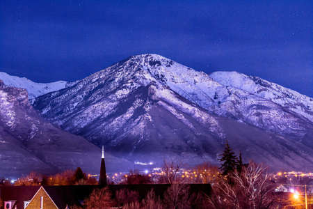 Snowy Wasatch Mountain towering over downtown Provo against blue evening sky. Scenic nature adn city landscape in Utah viewed at nighttime.の写真素材