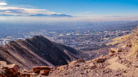 View over mountain peaks of Salt Lake City, Utah with a belt of haze or pollution blanketing the city under a blue skyの写真素材
