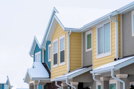 Townhome exterior with snowy gable valley roof against overcast sky in winter. Brick wall and colorful wall siding can also be seen at the exterior of this houses.の写真素材