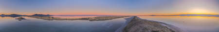 Sunset over the pans at the Bonnievale Salt Flats, Utah, USA with a fiery glow on the horizon reflected in the tranquil water in a very wide panorama landscapeの写真素材