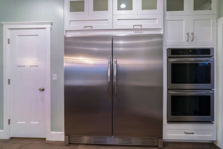 Large double door fridge with fitted ovens alongside in a modern home with white cabinetsの写真素材