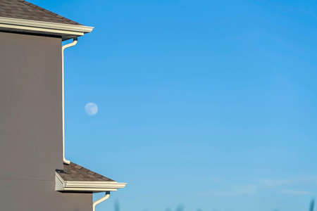 Close up of house exterior with blurry moon and blue sky in the background. The house has gray roof...