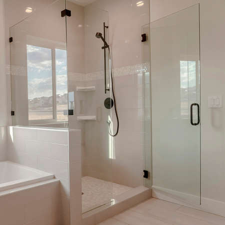 Square frame Built in bathtub with black faucet and shower stall with half glass enclosure. Interior of bathroom with view of snowy landscape and cloudy sky through the window.の写真素材