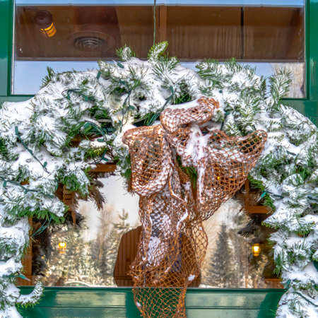 Square Snowy leafy wreath hanging on the glass wall of a building in Wasatch Mountains. The glass reflects a man standing amid scenic frosted landscape.の写真素材
