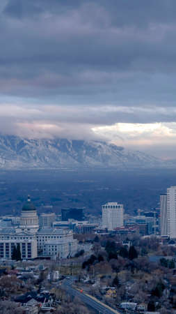 Vertical Downtown Salt Lake City with amazing view of steep snowy mountain in winter. Sky with thick gray clouds is over the gloomy urban and nature landscape.の写真素材