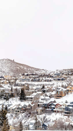 Vertical frame Park City Utah mountainscape with homes on a snowy neighborhood in winter. Picturesque residential and nature scenery with cloudy blue sky in the background.の写真素材
