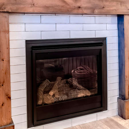 Square crop Modern fireplace with wooden frame against white accent wall of living room. Decorative mirror, ornamental jars, and flower vase can be seen above the fireplace.の写真素材