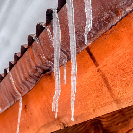 Square frame Icicles at the edge of corrugated metal roof with mound of fresh snow in winter. Close up of the snowy roofing of a building with wooden beams under the roof.の写真素材