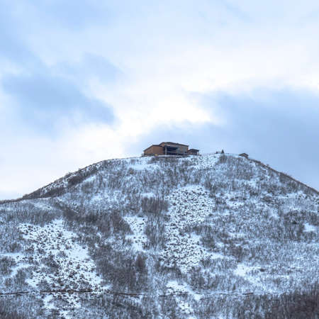 Square Homes built on the slopes of a hill overlooking cloud filled sky in winter. Abundant brown plants with no leaves thrive on the snow covered terrain.の写真素材