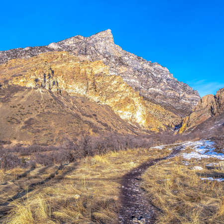 Square Trail on a grassy terrain with view of a rocky mountain in Provo Canyon Utah. Some fresh white snow can be seen on this sunny day.の写真素材