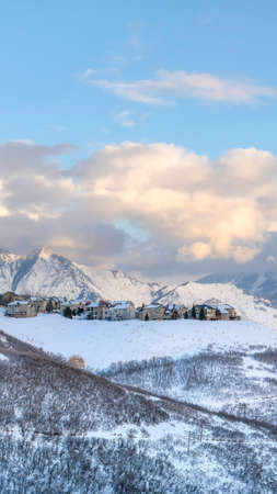 Vertical frame Panoramic view of homes situated amidst striking Wasatch Mountains in winter. The houses has an unobstructed views of snowy peaks and cloudy blue sky.の写真素材