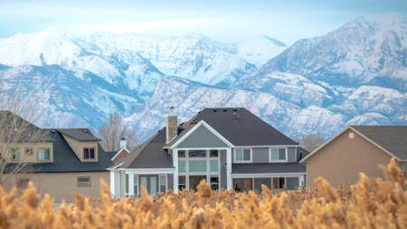 Panorama frame Homes and stunning snowy mountain with blurry brown grasses in the foregroundの写真素材