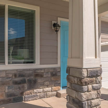 Square crop Arched entrance at the porch of home with blue front door beside window. Gray siding, stone brick wall, and arched garage door can also be seen at the facade of this house.の写真素材