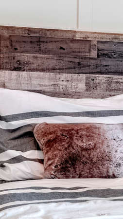 Vertical Bed with pillows against decorative wooden headboard against white panel wall. Bedroom interior of home with close up view of the single bed.の写真素材