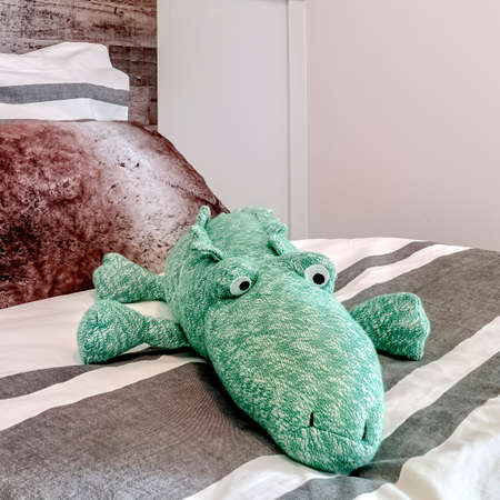 Square crop Single bed with wooden headboard against white bedroom wall with paneling. Pillows and animal stuffed toy is on the bed with striped beddings.の写真素材