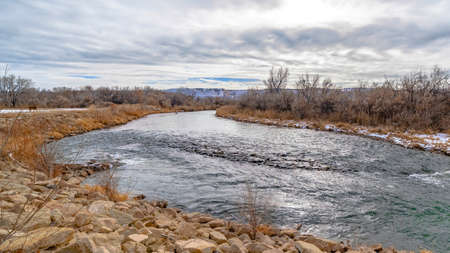 Panorama Glistening lake with dusting of snow on the rocky and grassy shore in winter. Mountain...