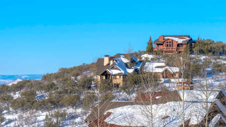 Panorama Park City Utah winter landscape with homes on a mountain top against blue sky. Evergreens...