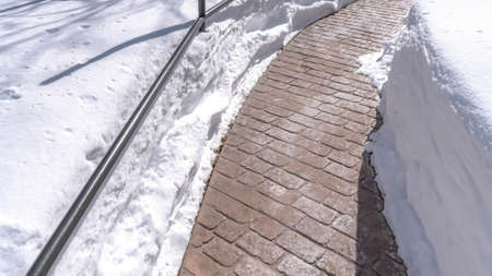 Panorama Stone brick pathway curving amid deep layer of fresh snow on a sunny winter day. Trees and home can also be seen in this scenic frosted landscape.の写真素材