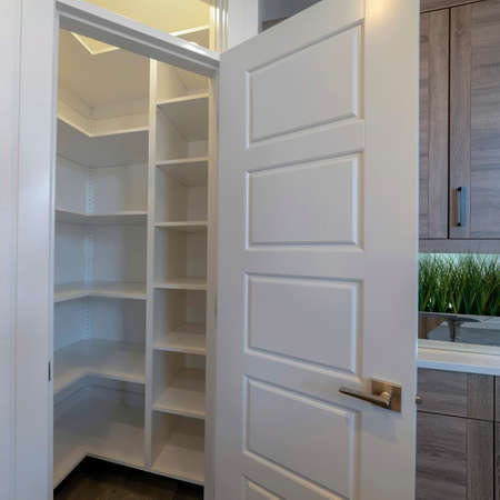 Square Small pantry with empty wall shelves at the corner of the kitchen of home. Door with transom window and cabinets can also be seen inside this room.の写真素材