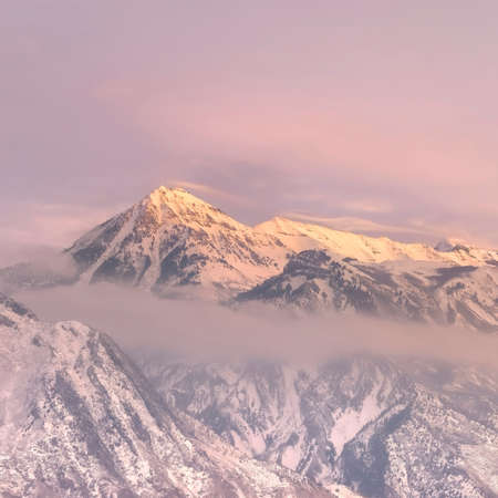 Square frame Snowy Wasatch Mountain and hill top towering over Utah Valley under cloudy sky. The steep peaks of the beautiful mountain is illuminated by golden sunset.の写真素材